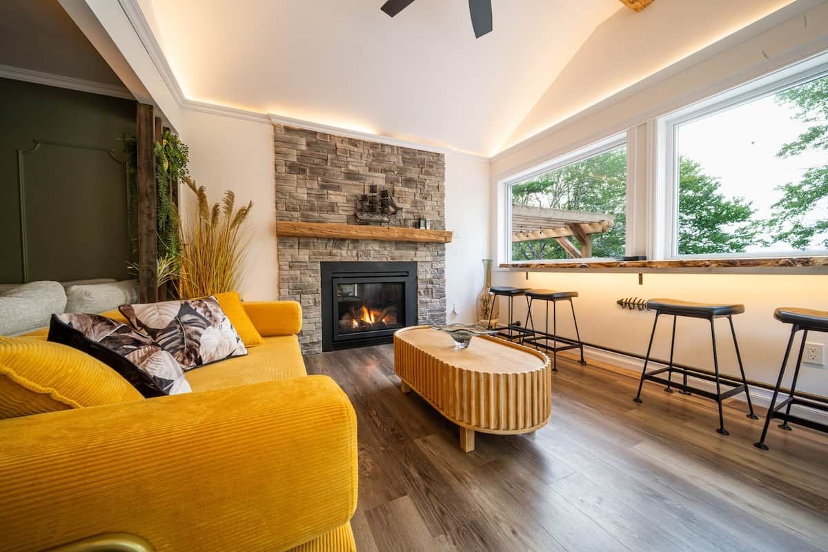Una sala de estar moderna con chimenea, sofá amarillo, mesa de centro de madera y una zona de bar con taburetes.