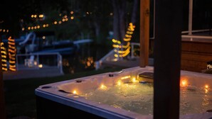 Un bain à remous avec vue sur une terrasse, le tout illuminé par des guirlandes lumineuses.