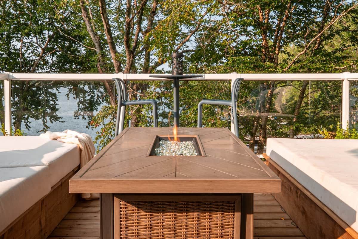Eine Terrasse mit Feuerstelle, zwei Betten und Blick auf ein Gewässer.