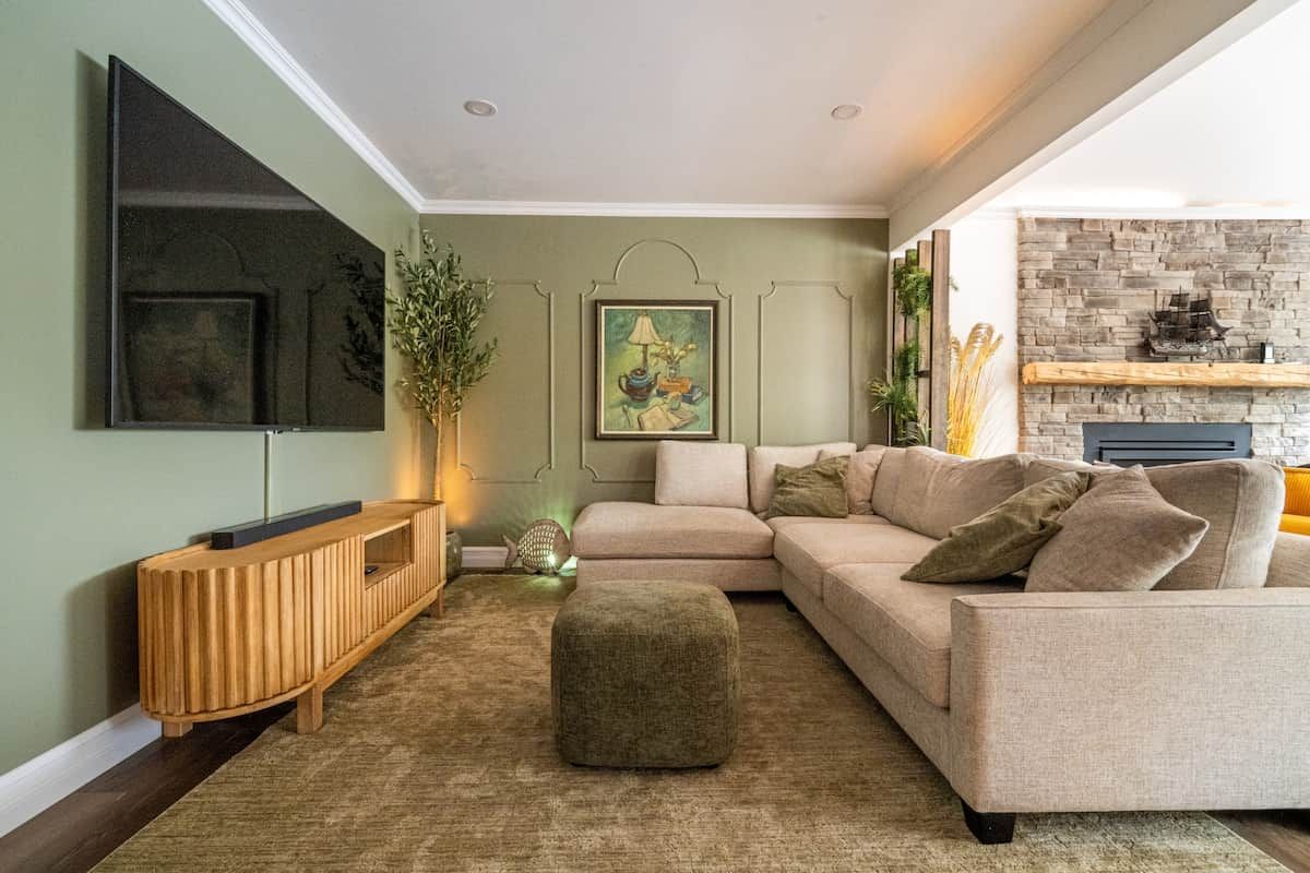 Ein Wohnzimmer mit einem Ecksofa, einem Holztischett, einem Flachbildfernseher, einem Kamin und einem Gemälde an der Wand.