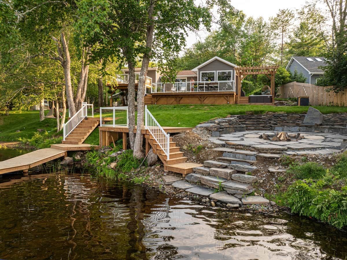 Una propiedad frente al lago con muelle de madera, escalones de piedra y una casa con terraza.
