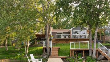 A wooden dock leading to a house with a deck and a staircase.