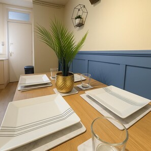 Een eettafel gedekt met witte borden, glazen en een potplant.