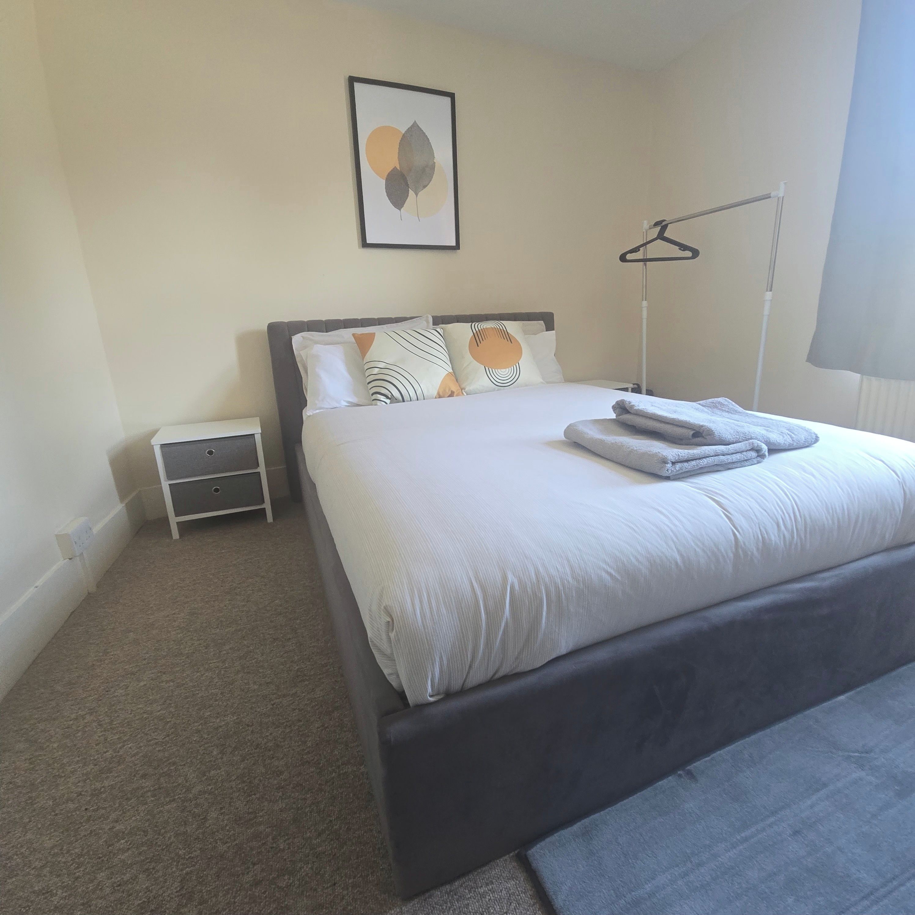 A neatly made bed with pillows and a folded towel, a bedside table with a lamp, and a framed artwork on the wall.