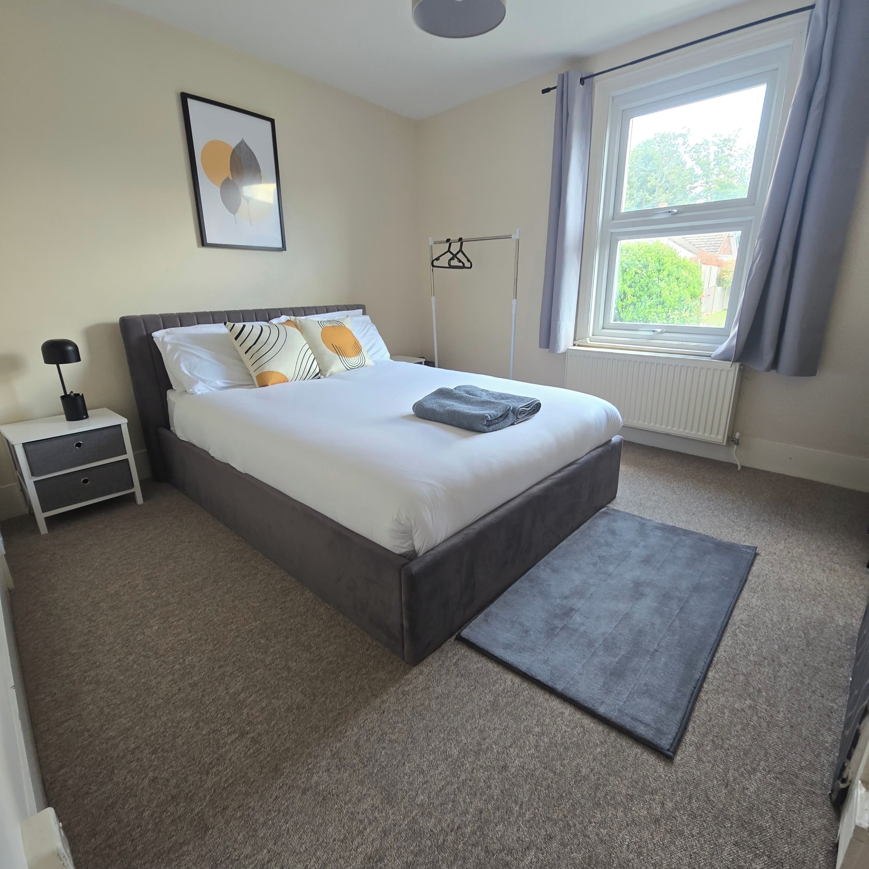 A bedroom with a bed, bedside table, lamp, and a window with curtains.