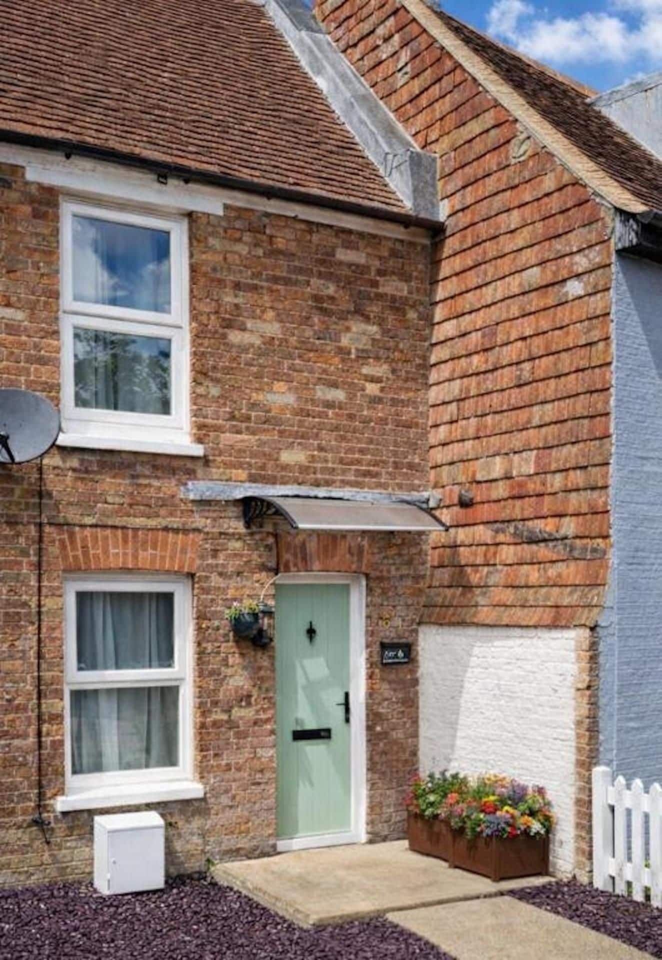 A two-story brick house with a green door, white-framed windows, and a satellite dish.