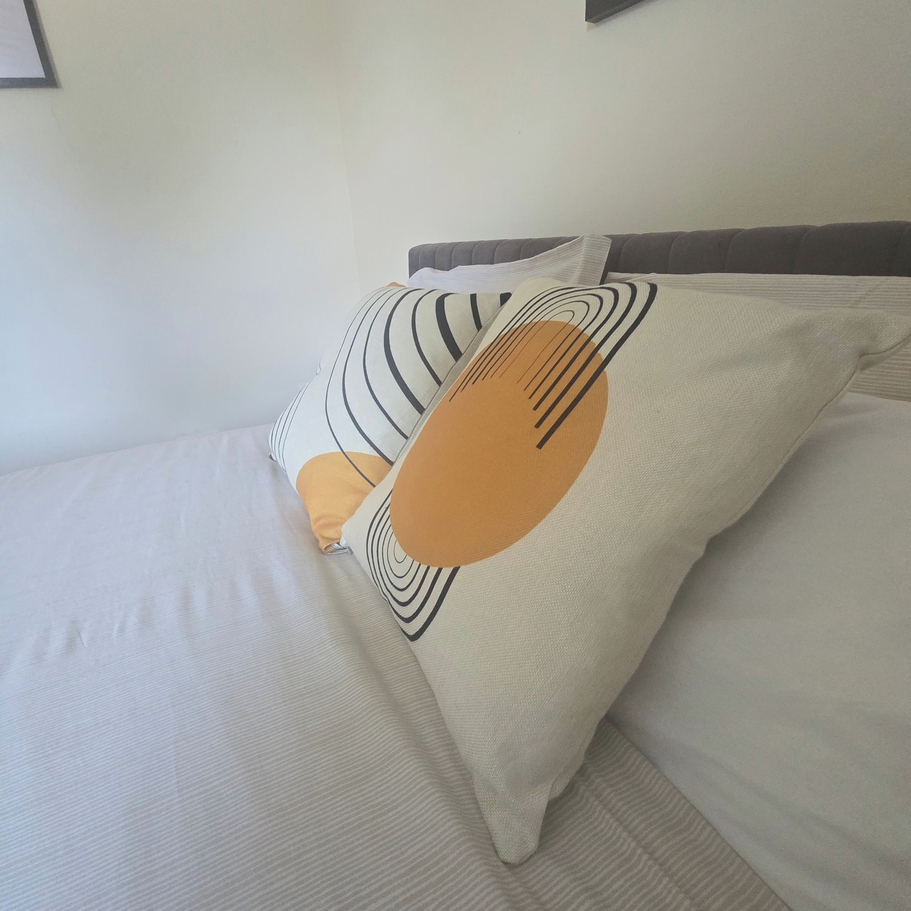 A bed with a white mattress and two pillows with abstract designs.