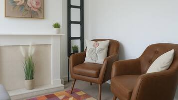 Sala de estar com lareira, dois poltronas de couro marrom, tapete colorido, relógio e quadro com flores emolduradas.