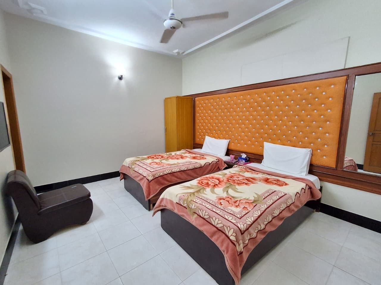 Habitación de hotel con dos camas, ventilador de techo y una silla.