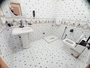 Baño con lavamanos, inodoro y ducha blancos. El piso presenta un diseño de rombos.