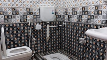 A small bathroom with a toilet, bidet, and sink. The walls are tiled with a geometric pattern.