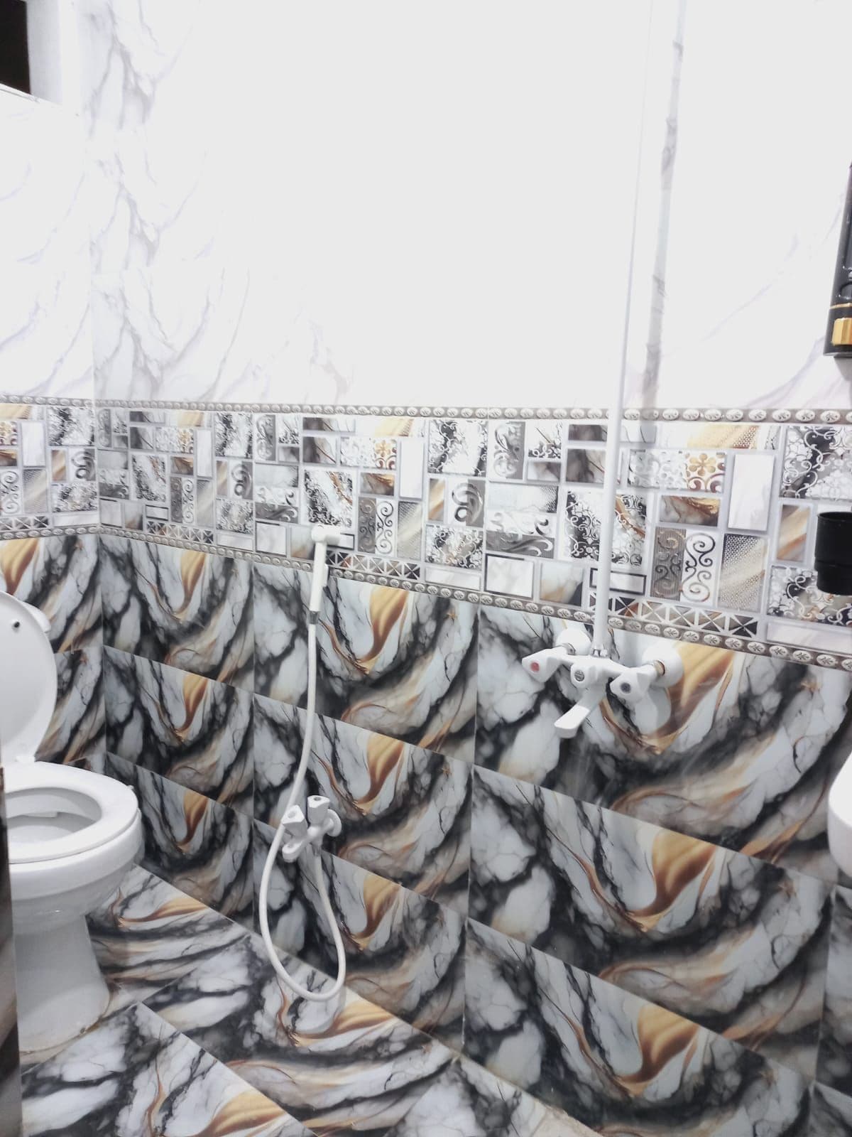 A bathroom with a marble-like tile design on the walls and floor, a white toilet, and a shower area.