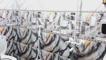 A bathroom with a marble-like tile design on the walls and floor, a white toilet, and a shower area.