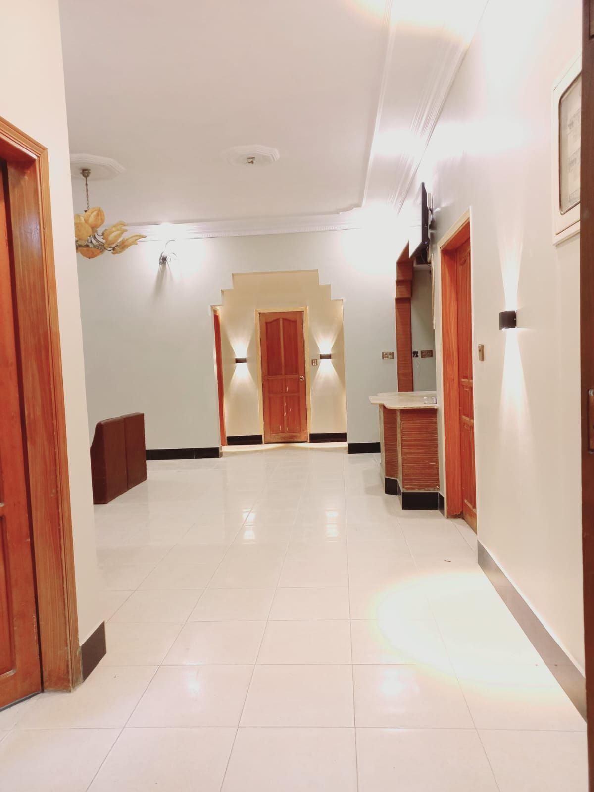 A hotel hallway with a tiled floor, wooden doors, and a central staircase.