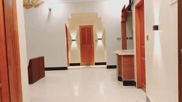 A hotel hallway with a tiled floor, wooden doors, and a central staircase.