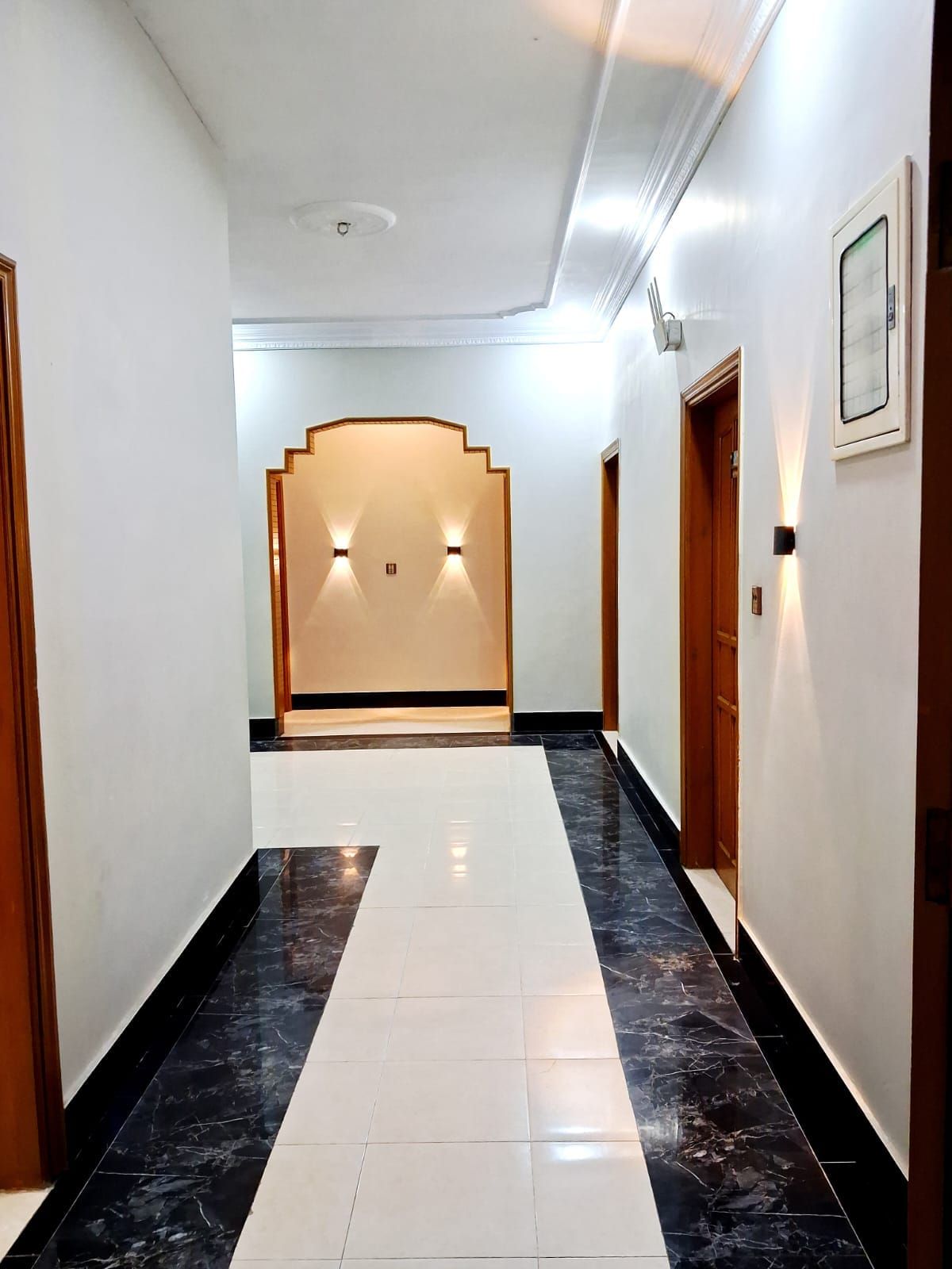 A hallway with a marble floor, white walls, and wooden doors.