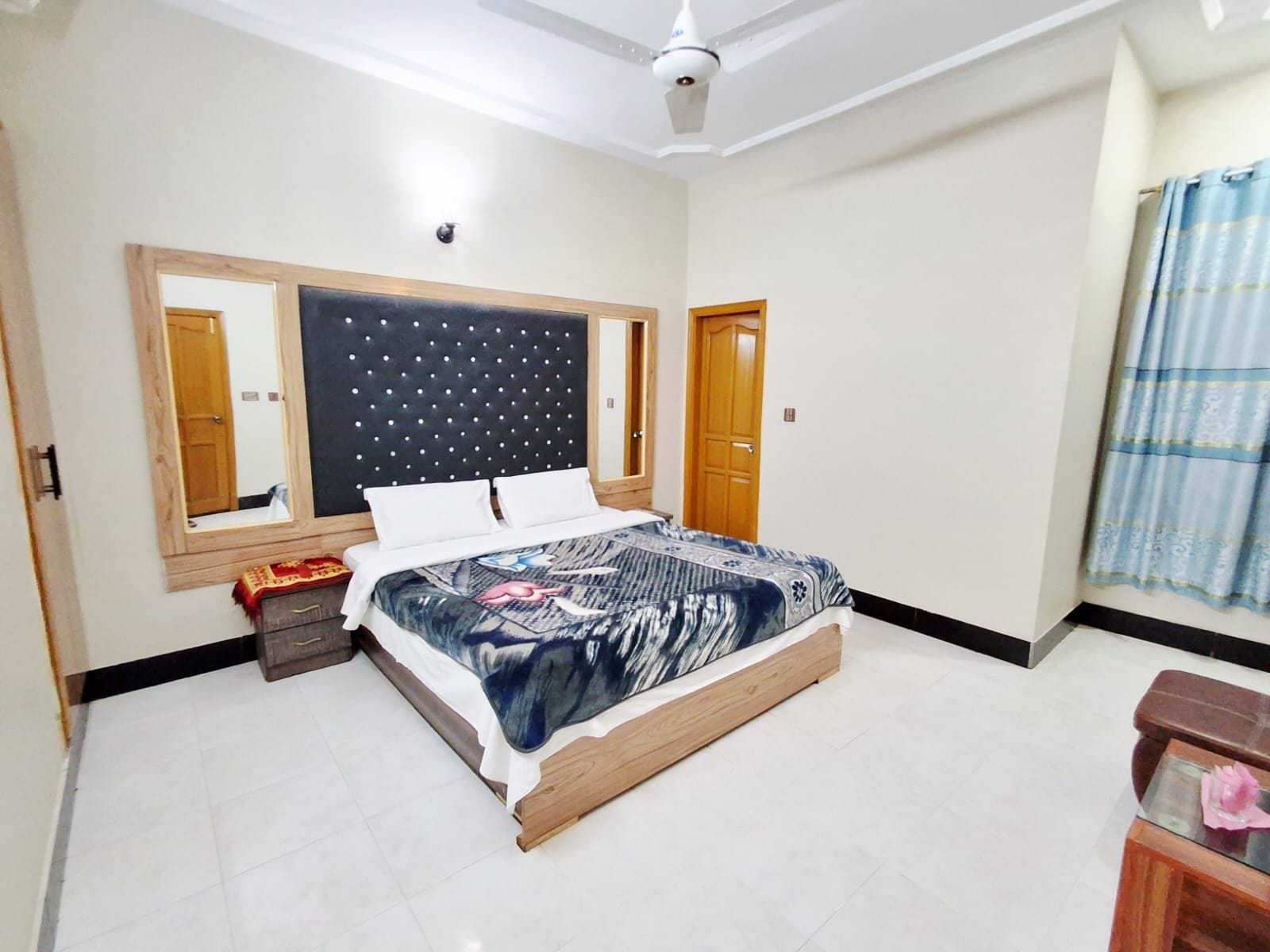A bedroom with a bed, a ceiling fan, a mirror, and a door.