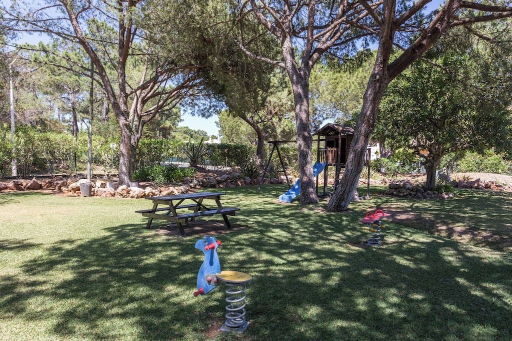 A park with picnic tables, playground equipment, and a small wooden structure.