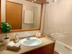 Un bany amb un penjador de fusta, un rentapeus blanc, un mirall, una cabina de dutxa de vidre i una planta en test.