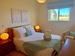 Ein Schlafzimmer mit Bett, Nachttisch, Lampe, Fenster mit Ausblick und einem Sessel.