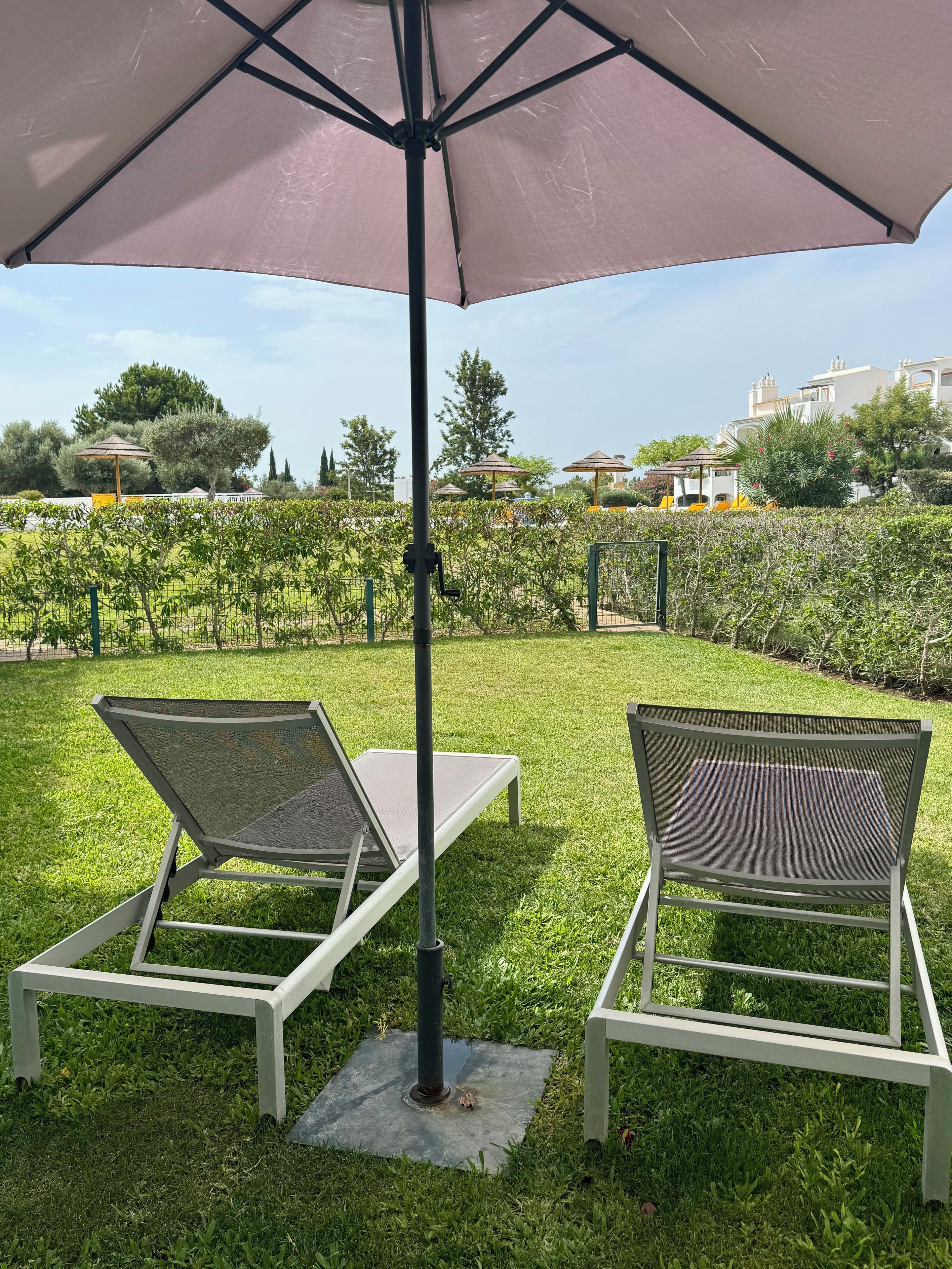 Deux fauteuils de jardin placés sous un grand parasol, dans un espace extérieur verdoyant, avec un vignoble en arrière-plan.