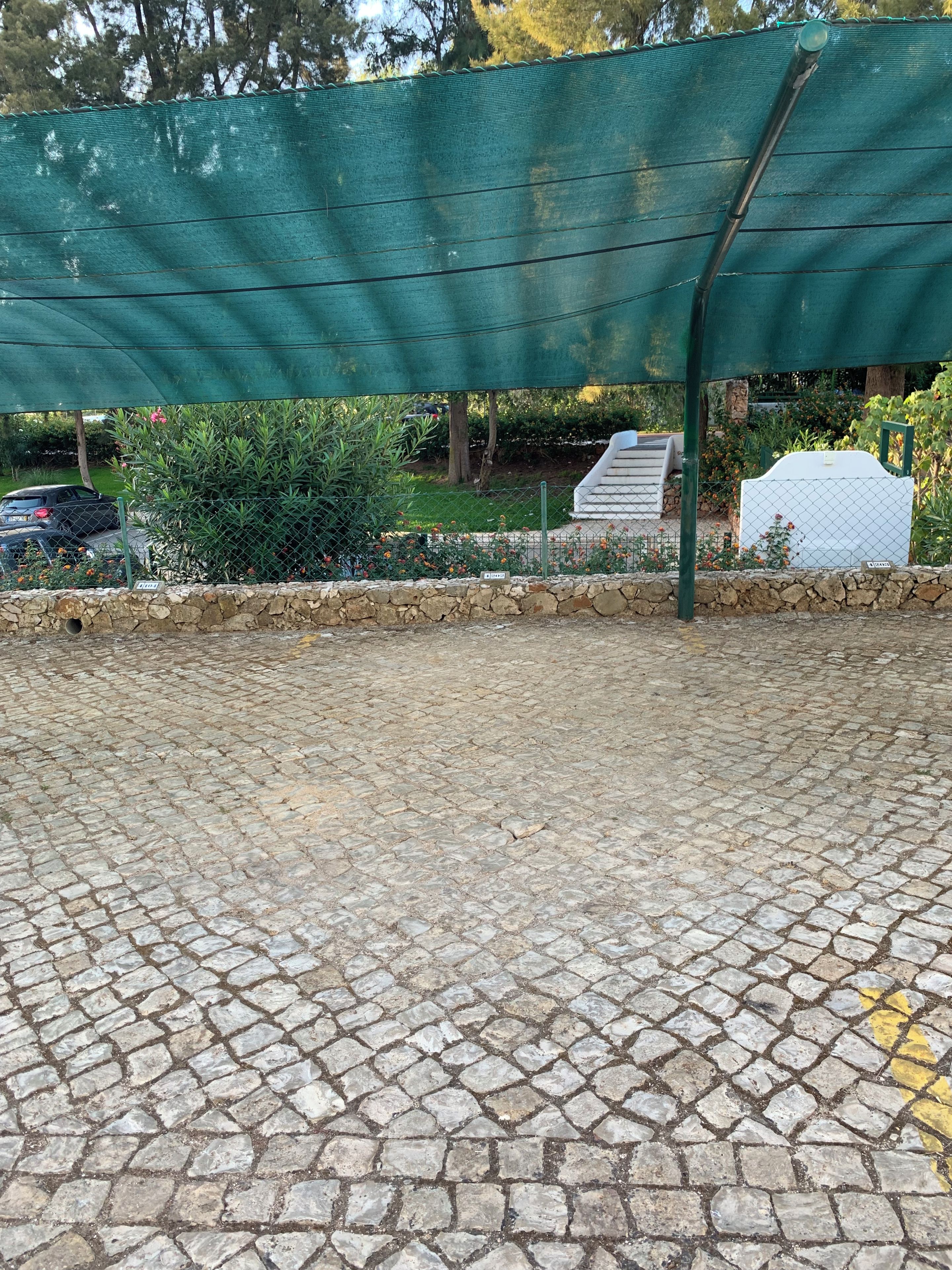 A paved area with a stone pattern, a green fence, and a white structure in the background.