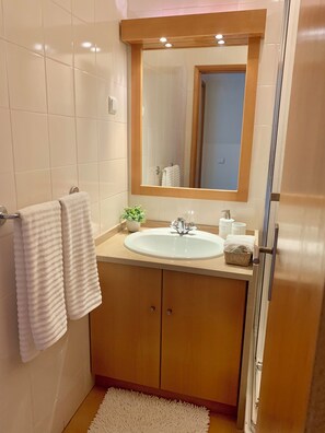 Ein Badezimmer mit einem weißen Waschbecken, Holzschränken, einem Spiegel und einer Duschkabine aus Glas.