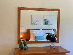 A bedroom with a wooden headboard, a bedside table with a potted plant, and two framed artworks on the wall.