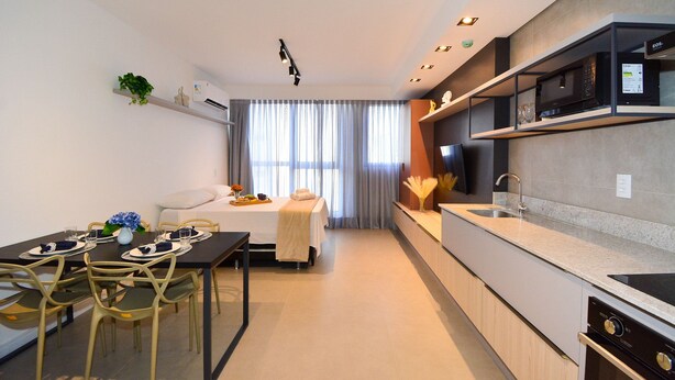 Una cocina moderna con microondas integrado, un comedor con mesa y sillas, y una cama con cubrecama blanco.