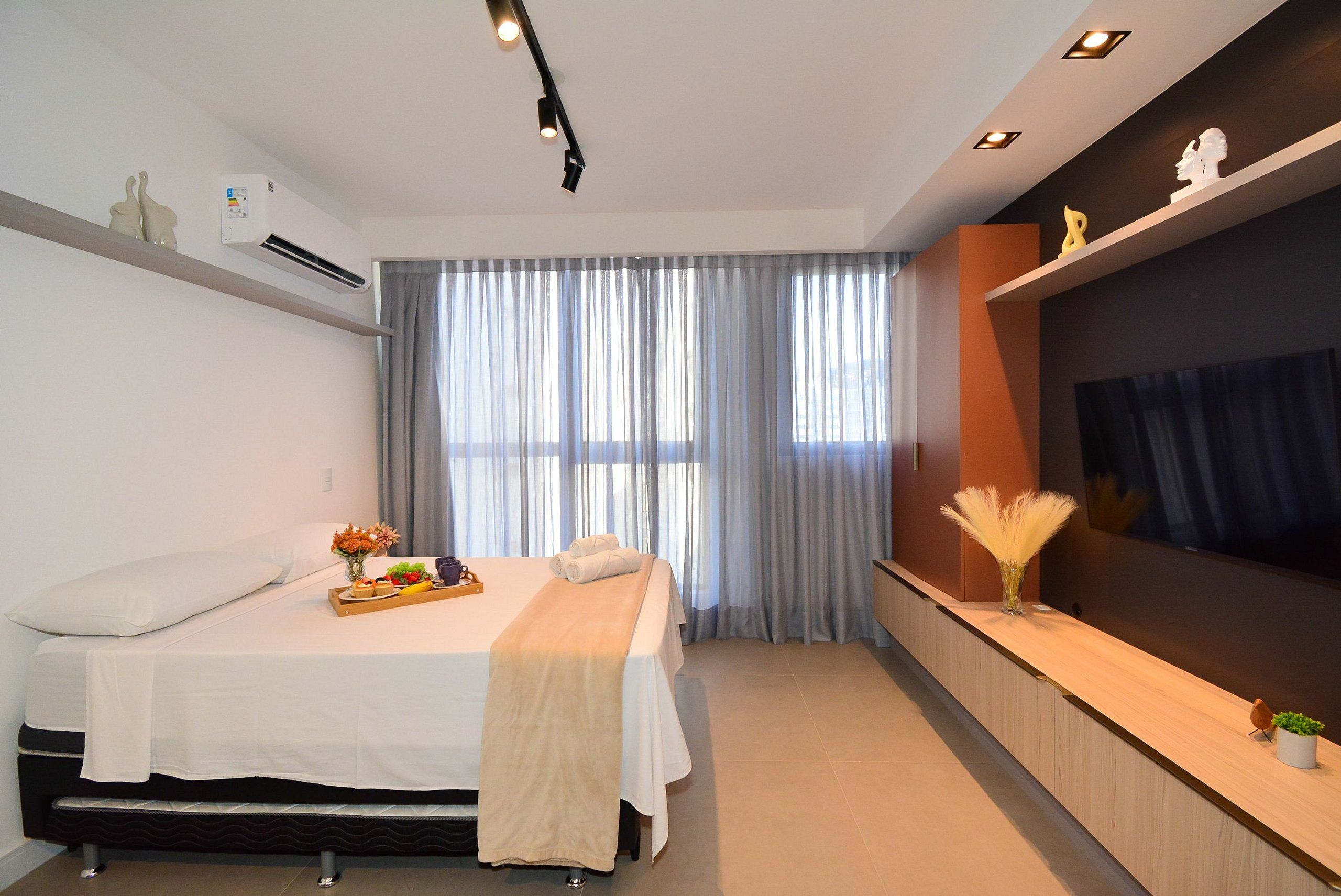 A modern hotel room with a bed, bedside table, air conditioning unit, and a large window with curtains.