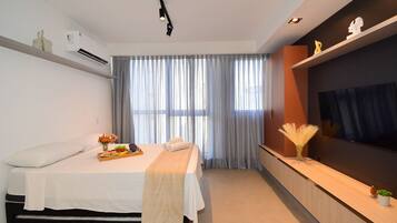 A modern hotel room with a bed, bedside table, air conditioning unit, and a large window with curtains.