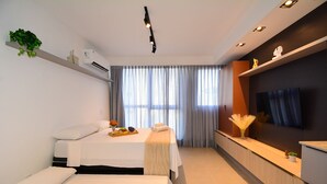 Una habitación de hotel con cama, mesita de noche, televisor y ventana con cortinas.