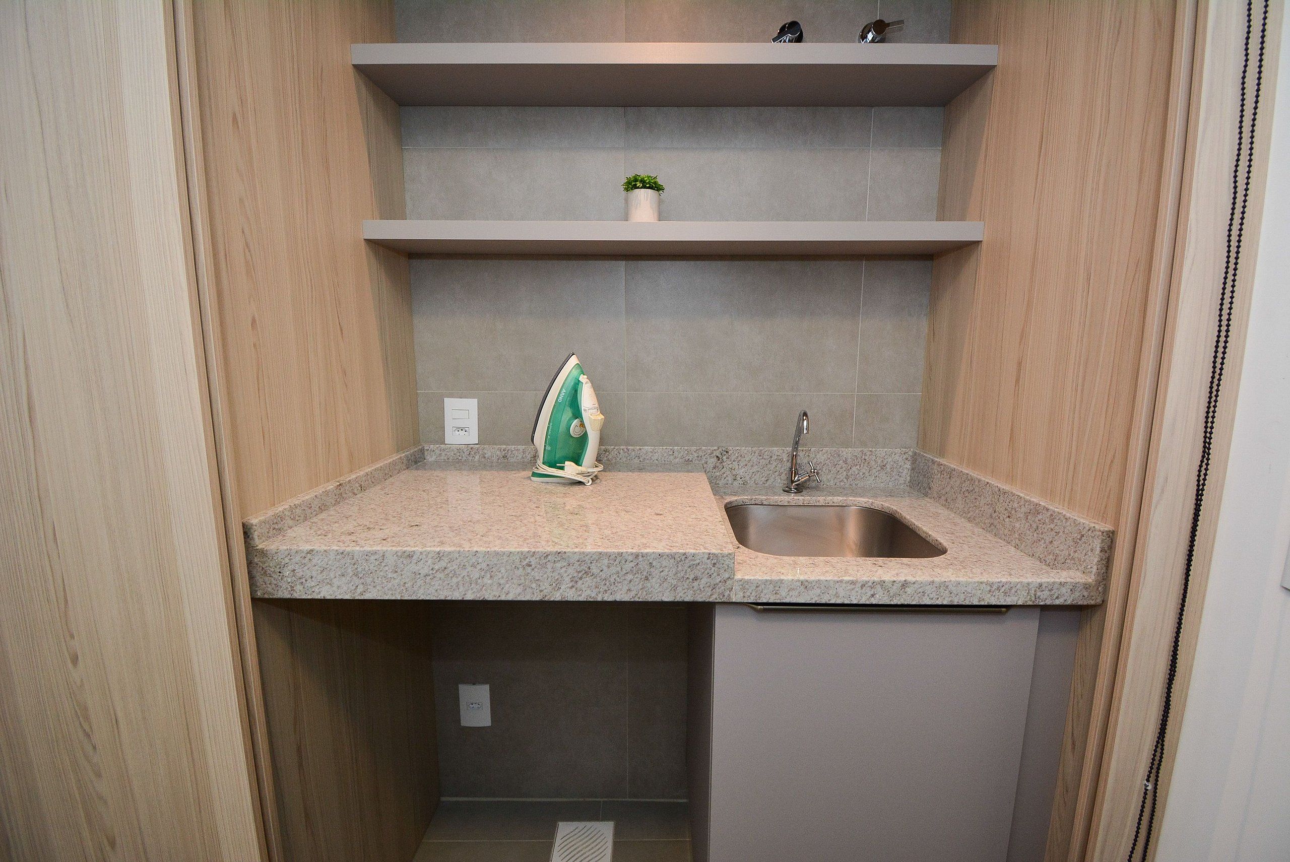 A compact kitchen with a granite countertop, a stainless steel sink, and a small potted plant on a shelf.