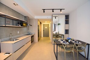 A modern kitchen with a built-in oven, a sink, and a dining area with a table set for four. - Studio em frente a UFSC e HU - 508A (Florianópolis)