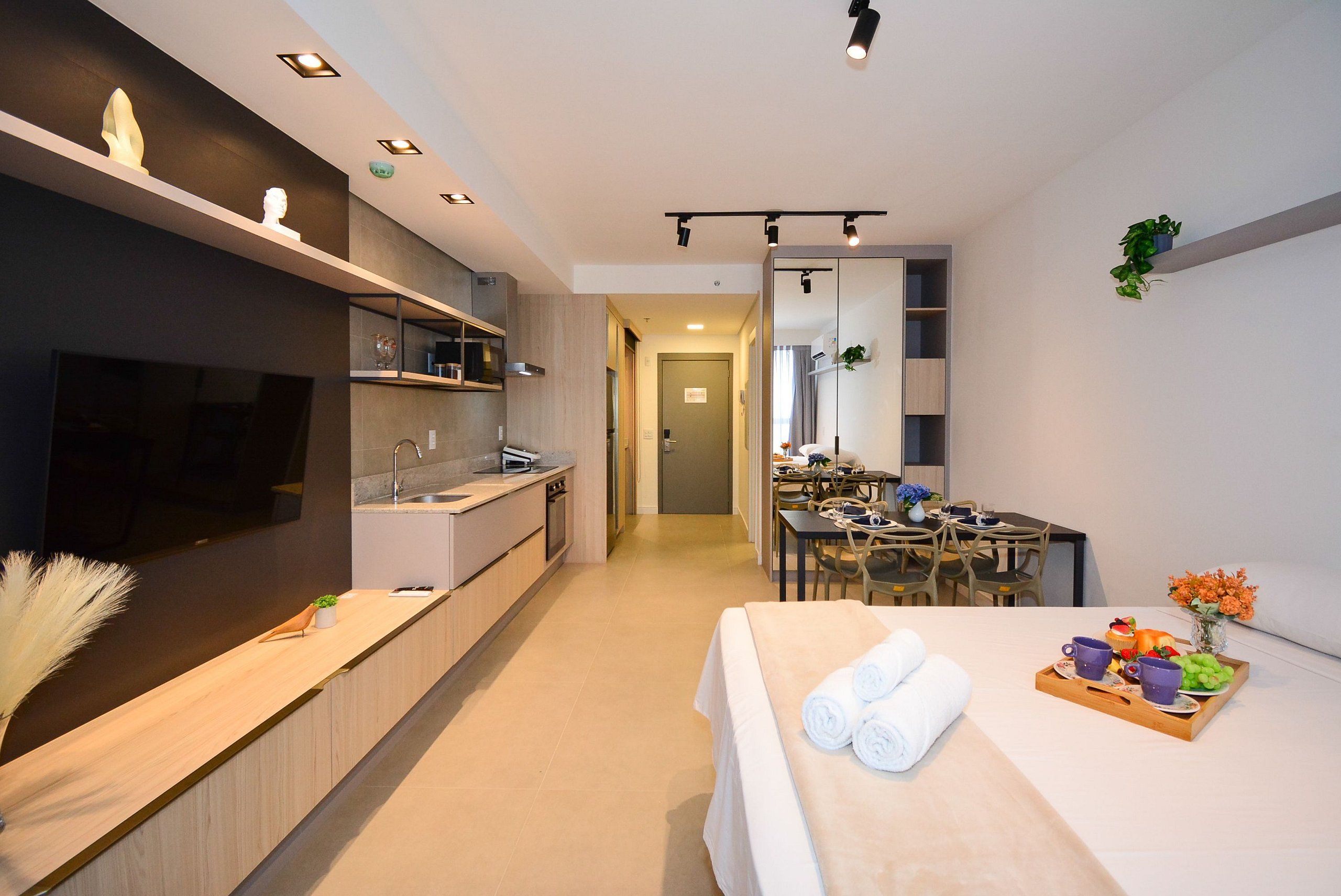 Habitación de hotel moderna con cocina, comedor y una cama con toallas y fruta.