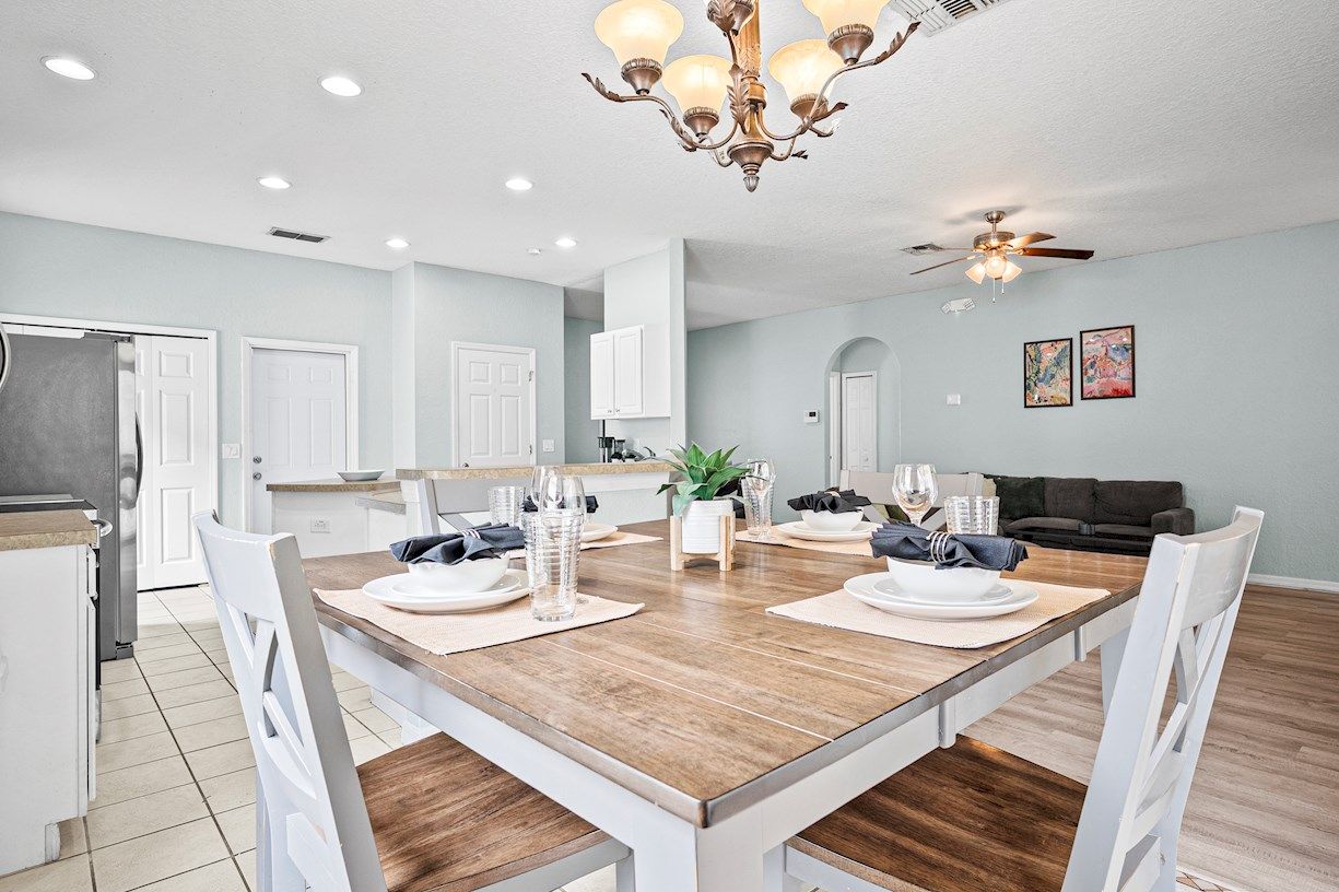A dining area with a wooden table set for four, surrounded by white chairs.