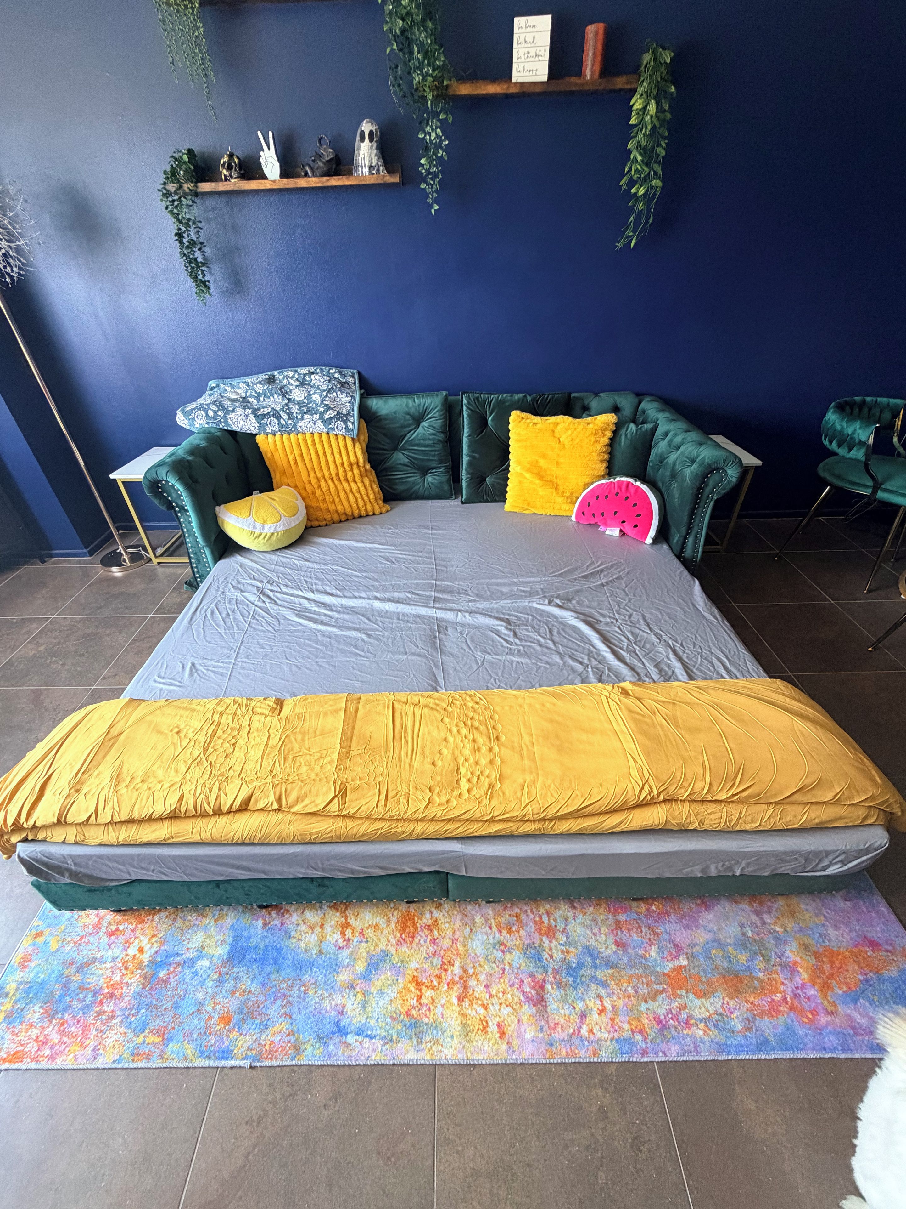 A bed with a colorful mattress, a green upholstered headboard, and a vibrant throw blanket.