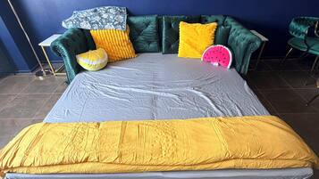 A bed with a colorful mattress, a green upholstered headboard, and a vibrant throw blanket.