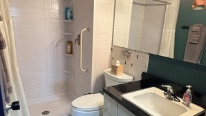 A bathroom with a shower, toilet, sink, and a towel rack. - Midtown Omahas, The Good Life Loft with view of downtown (Omaha)