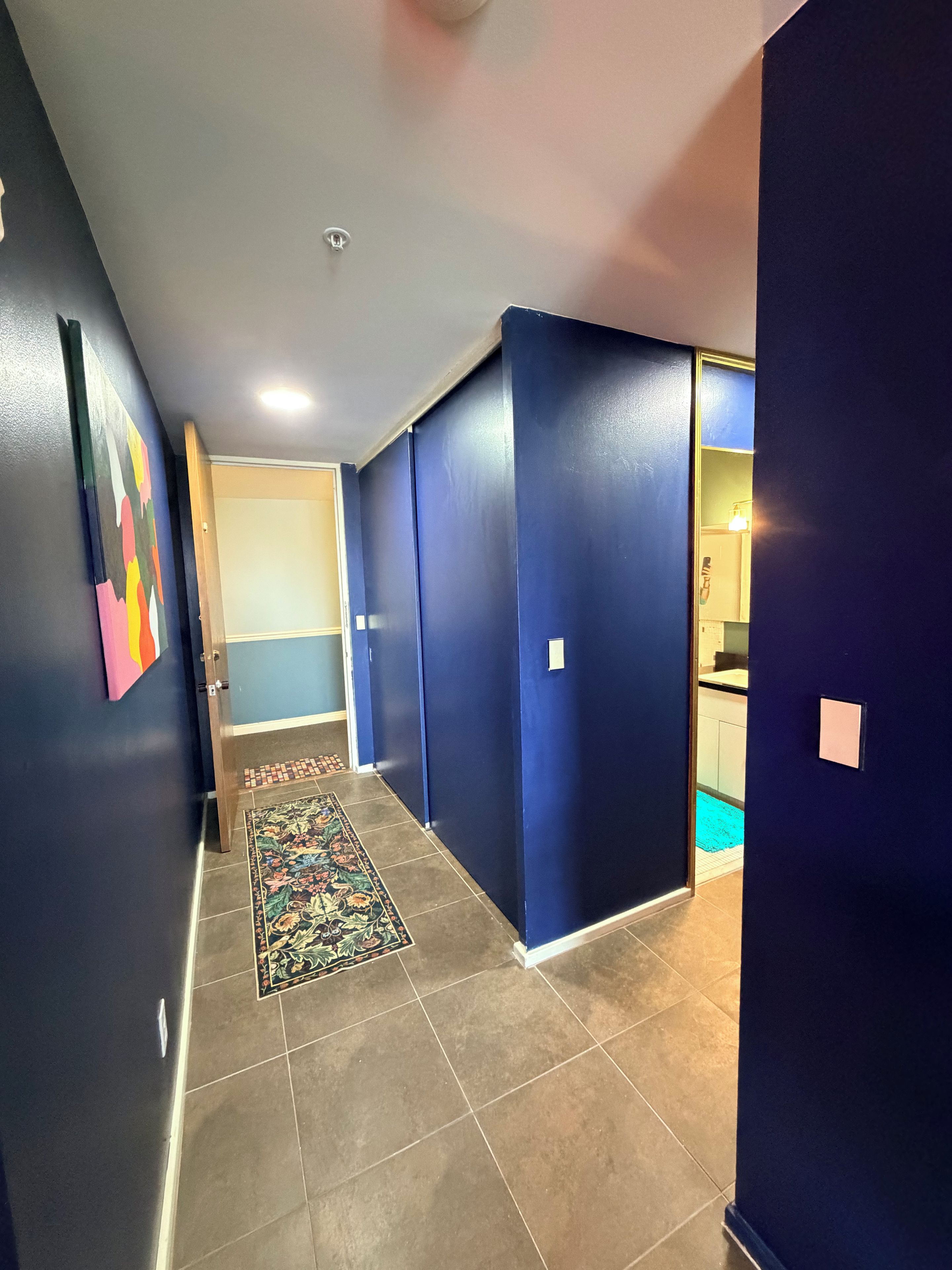 Un couloir aux murs bleus, orné d’un tapis à motifs et dont une porte donne sur un espace cuisine.