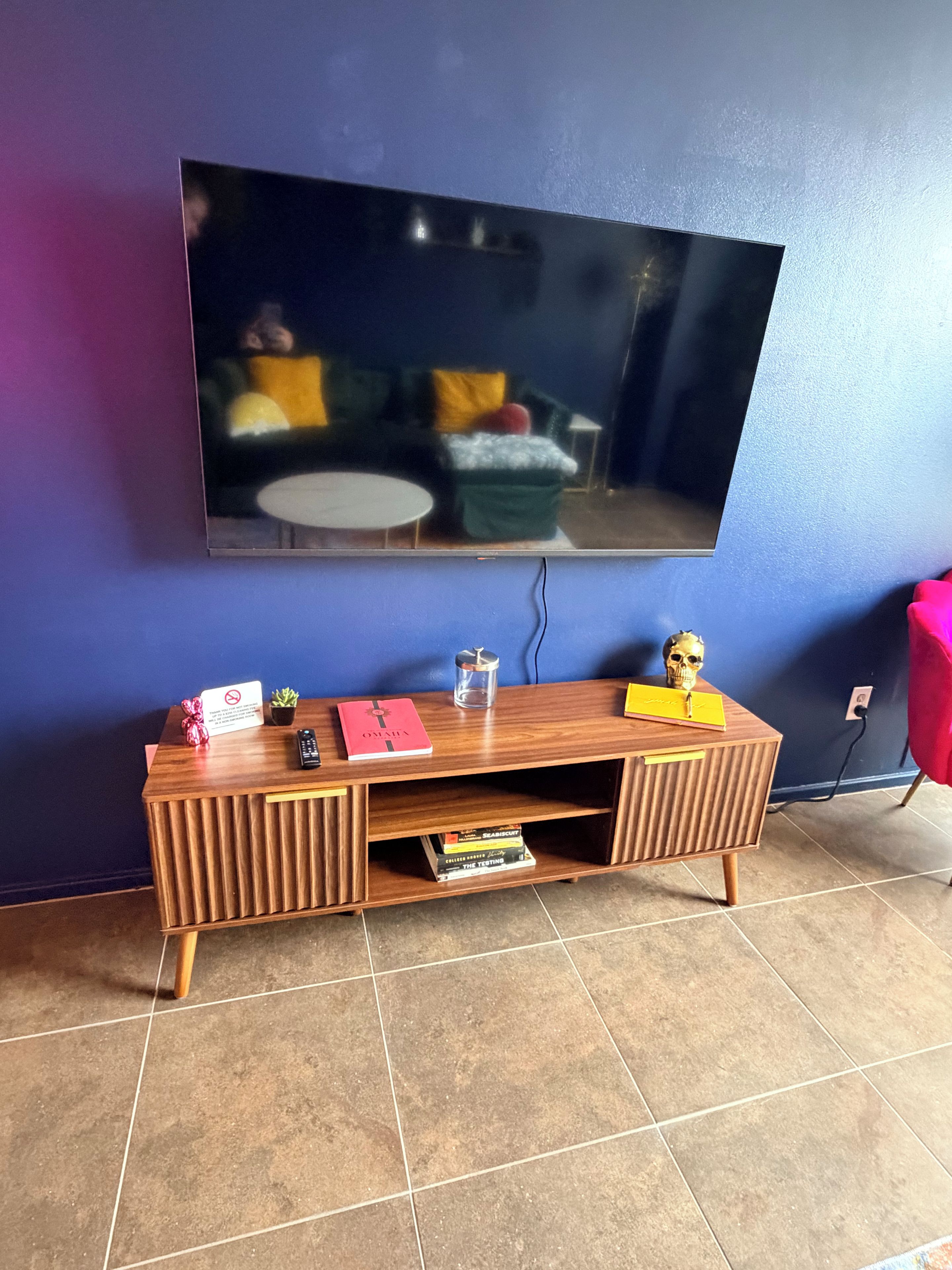 A room with a wooden entertainment unit, a flat-screen TV mounted on the wall, and a tiled floor.
