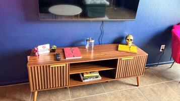 A room with a wooden entertainment unit, a flat-screen TV mounted on the wall, and a tiled floor.