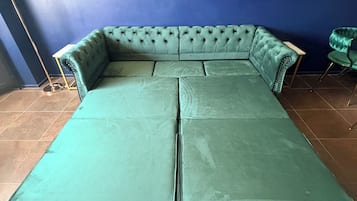 A teal sectional sofa with a tufted design, a colorful rug, and decorative plants on shelves against a blue wall.