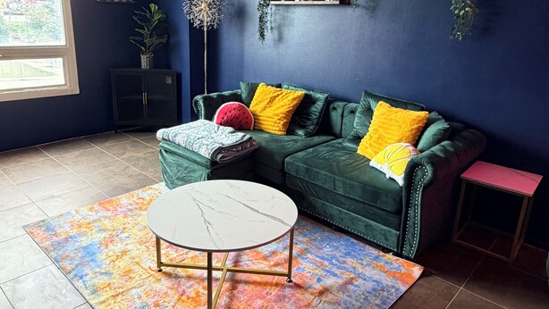A living room with a dark blue wall, a green sofa with yellow cushions, a round coffee table, and a colorful rug. - Midtown Omahas, The Good Life Loft with view of downtown (Omaha)