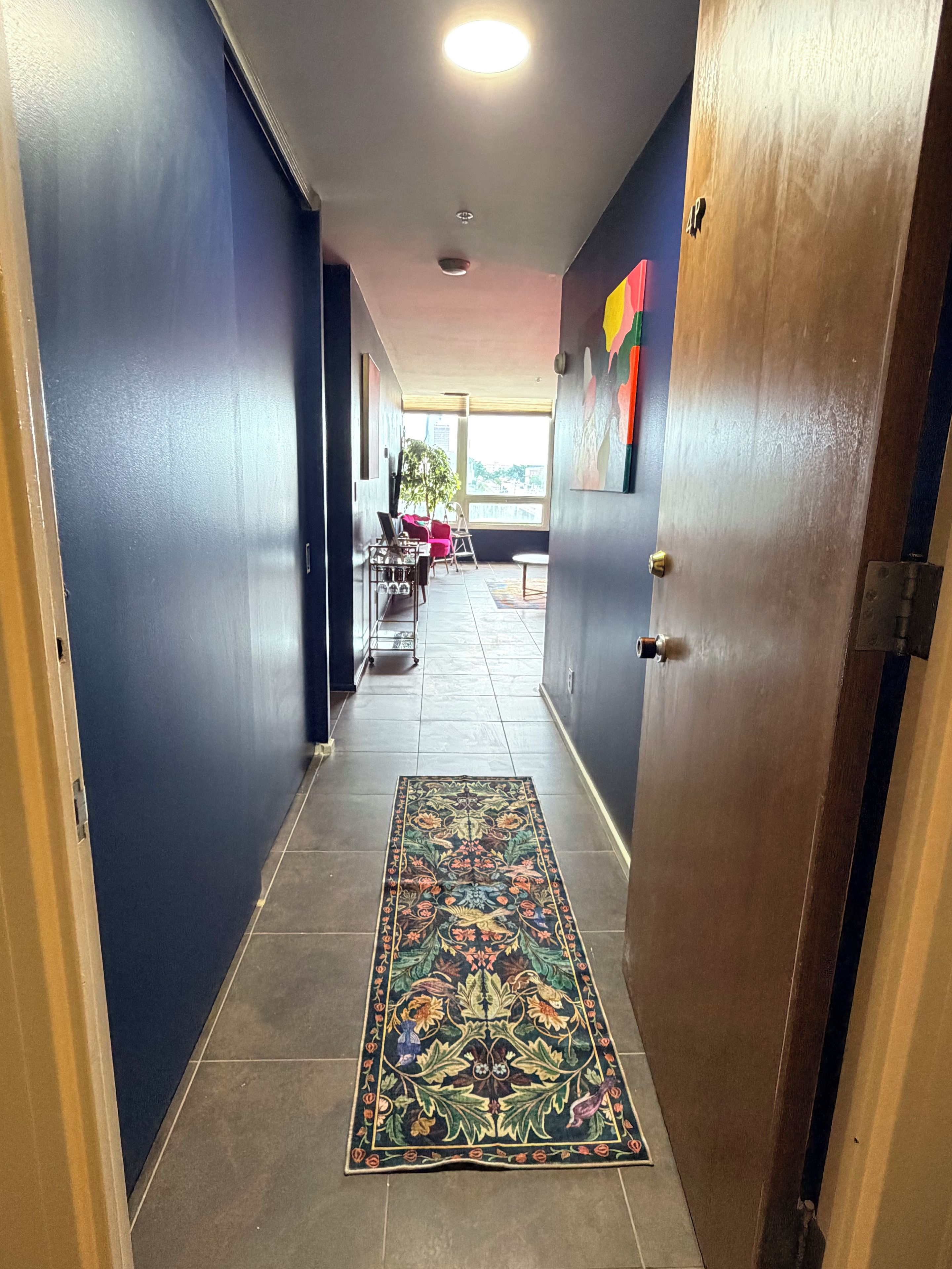 A hallway with a patterned rug, a door, and a view of an outdoor area with a table and chairs.