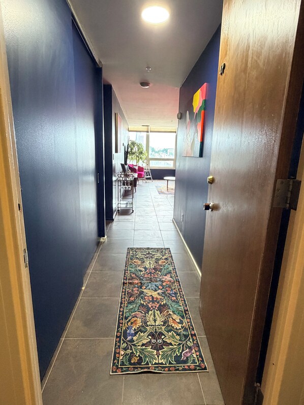 A hallway with a patterned rug, a door, and a view of an outdoor area with a table and chairs.