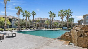 A swimming pool with lounge chairs and palm trees, surrounded by buildings. - Sleepover | Relaxing 1BD/1BA+ Gym - Corpus Christi (Corpus Christi)