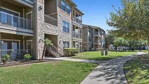 A multi-story residential building with balconies, a stone facade, and a well-maintained lawn. - Sleepover | Relaxing 1BD/1BA+ Gym - Corpus Christi (Corpus Christi)
