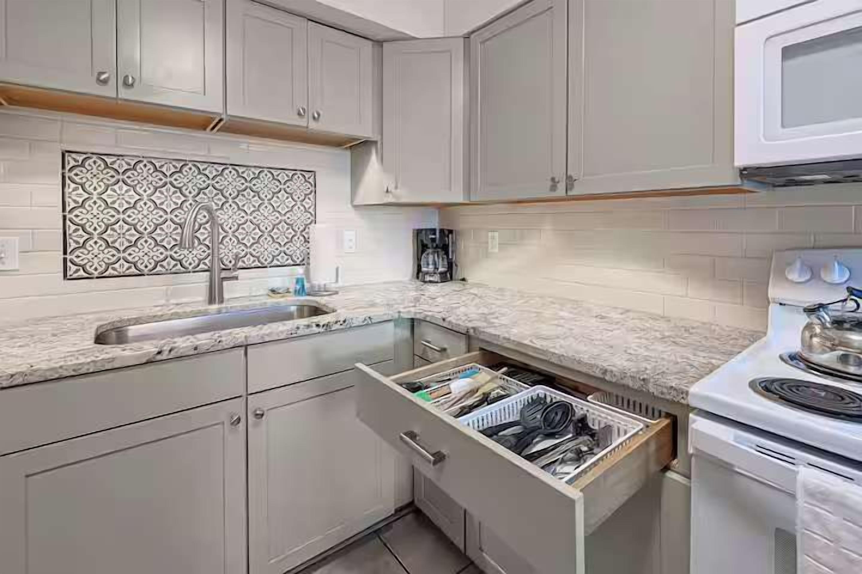 A kitchen with white cabinets, a patterned backsplash, a sink, and a stove.