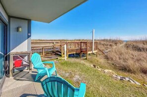 Ein Strandhaus mit einer Terrasse, Gartenstühlen und einer Holztreppe zum Strand.